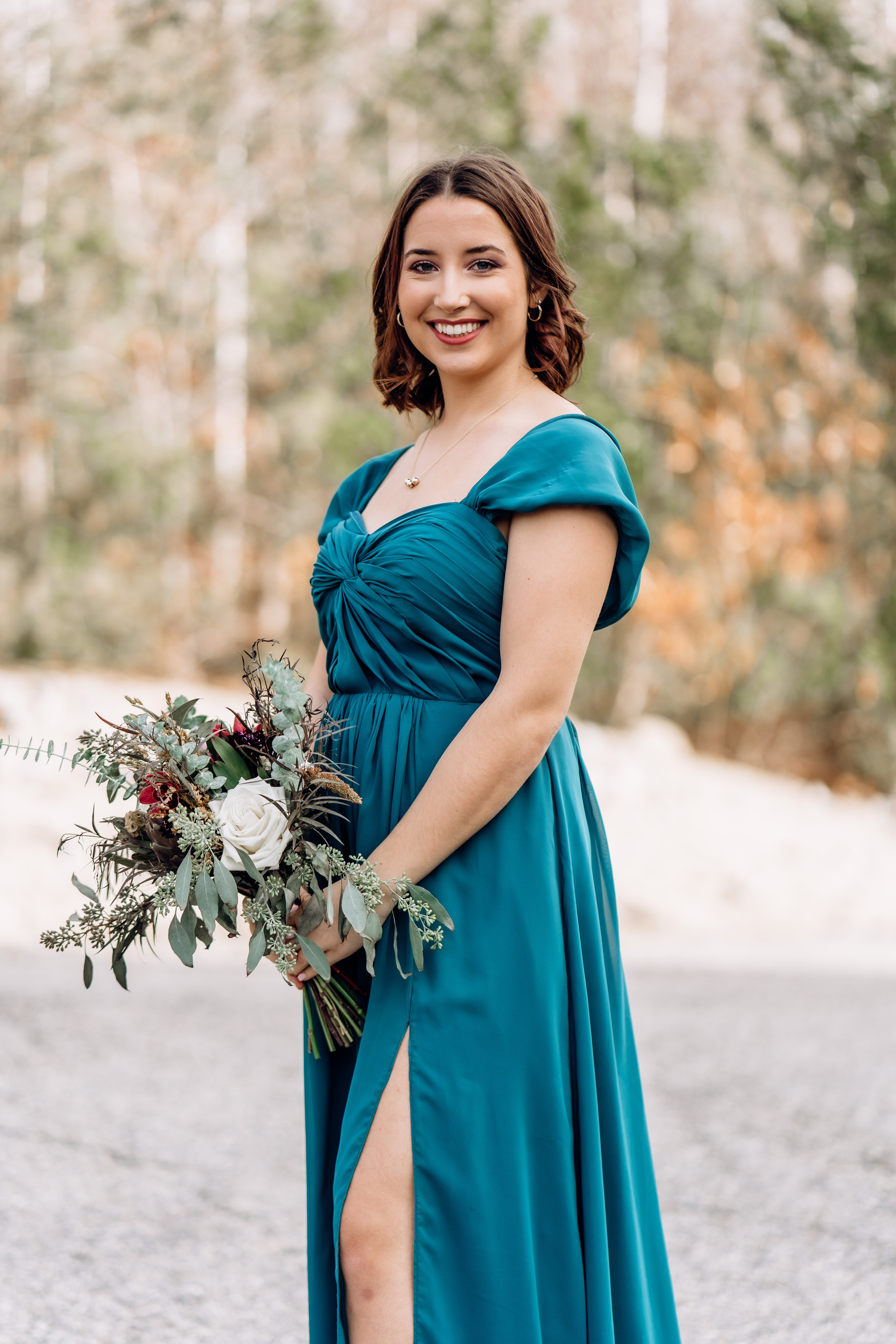 Sarah Quattrucci — portrait outdoors in a teal off-shoulder dress, holding a bouquet of white roses and eucalyptus.
